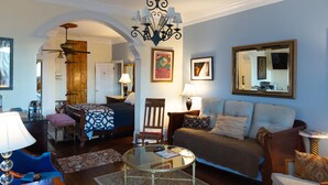 A living room with a glass coffee table, a sofa, a chair, and a small table with a lamp. There is a mirror on the wall and a door leading to another room. - Blue60 Marigny Inn (New Orleans)