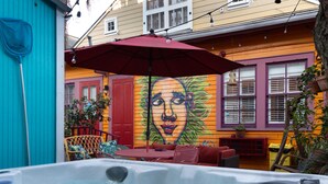 A hot tub area with a mural, outdoor seating, and a red umbrella. - Blue60 Marigny Inn (New Orleans)