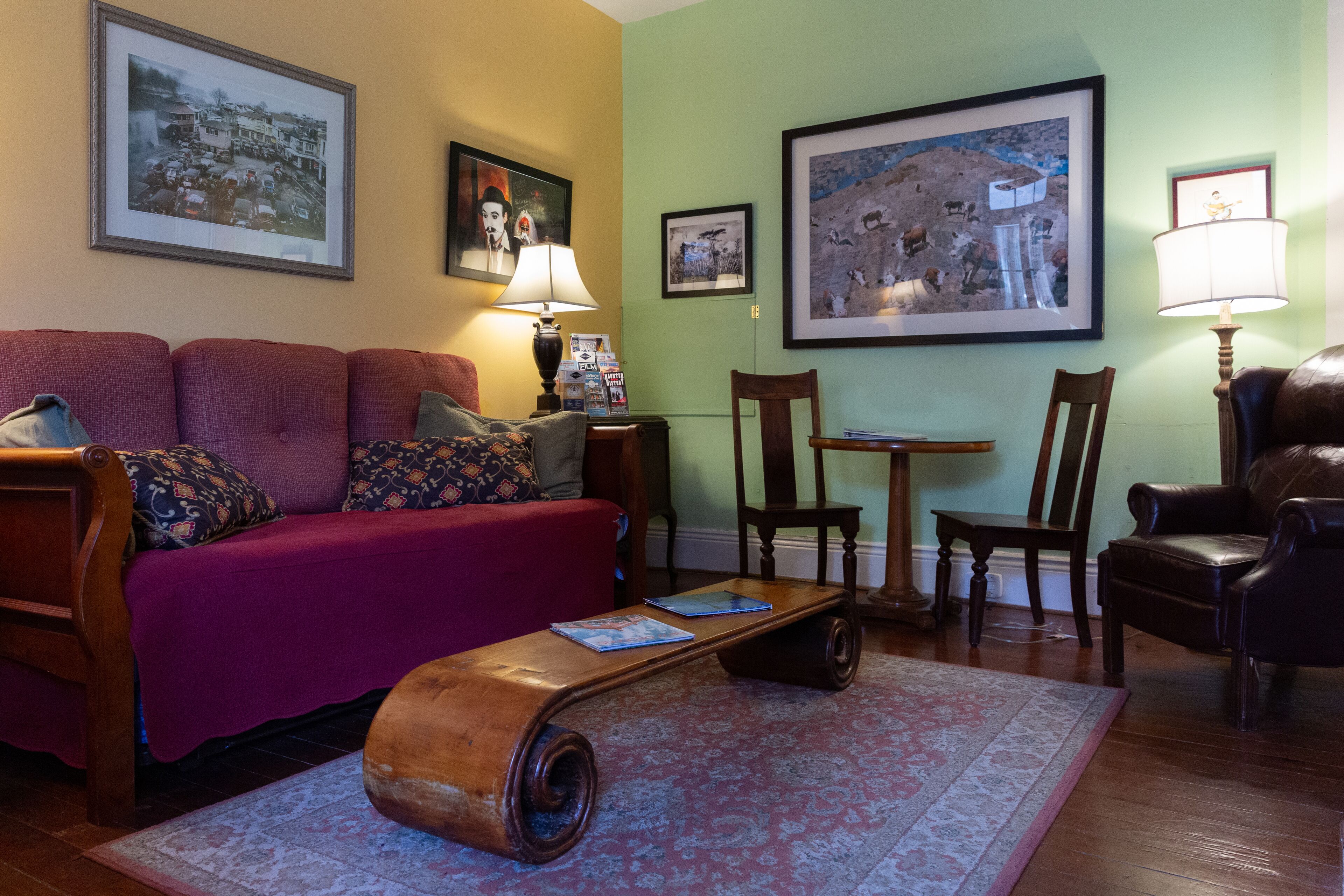 A living room with a red sofa, wooden coffee table, and a patterned rug. There are framed pictures on the walls and a lamp on a side table.