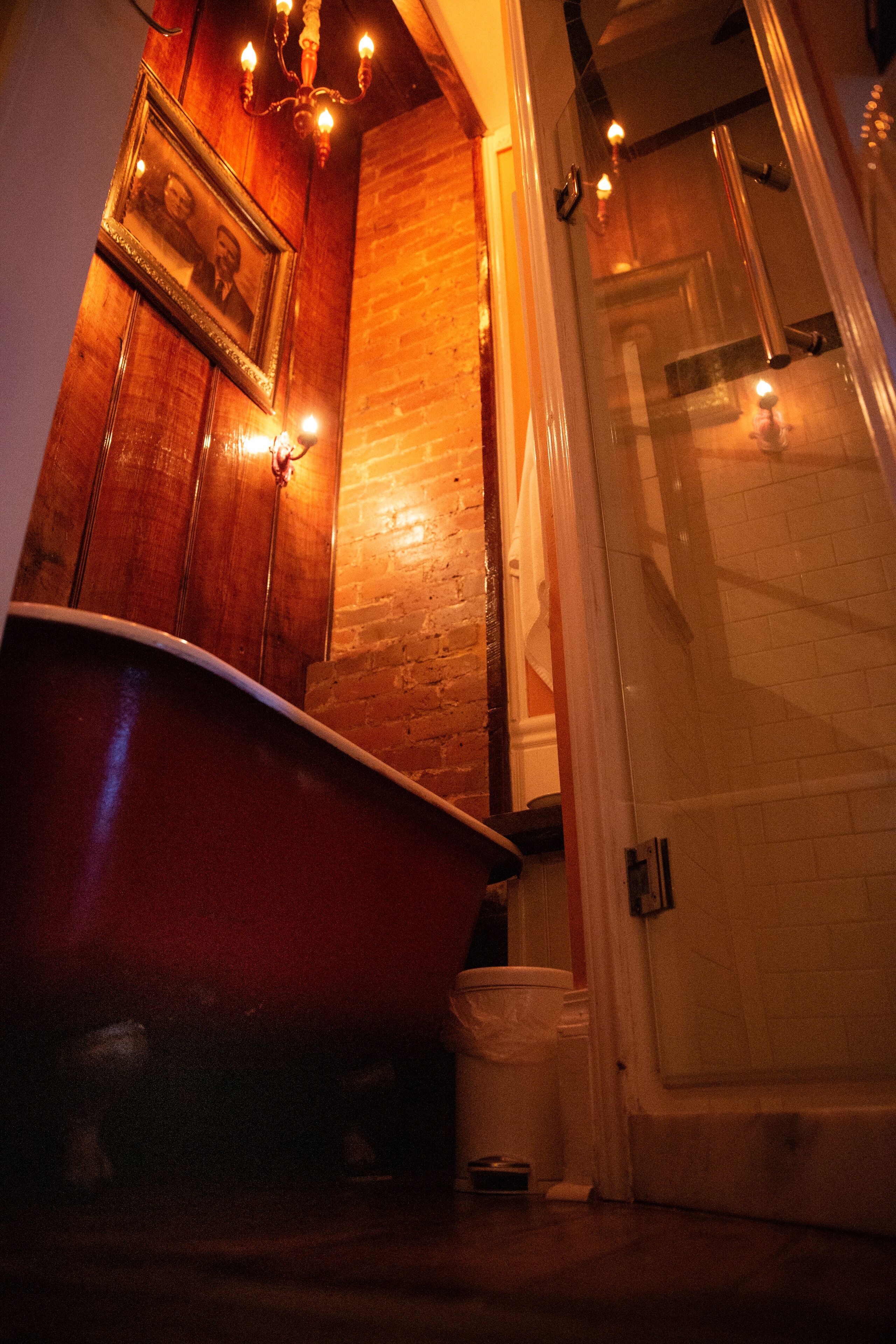 A bathroom with a wooden vanity, a red bathtub, and a glass shower enclosure.