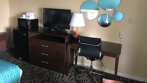 A hotel room with a TV, coffee maker, microwave, wooden desk, chair, and decorative wall mirrors.