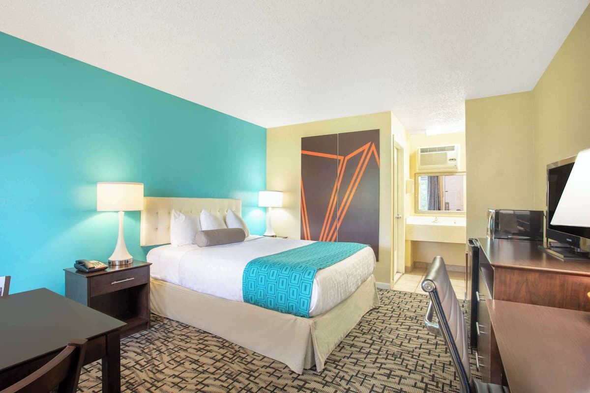 A hotel room with a bed, bedside tables, a desk, and a television.