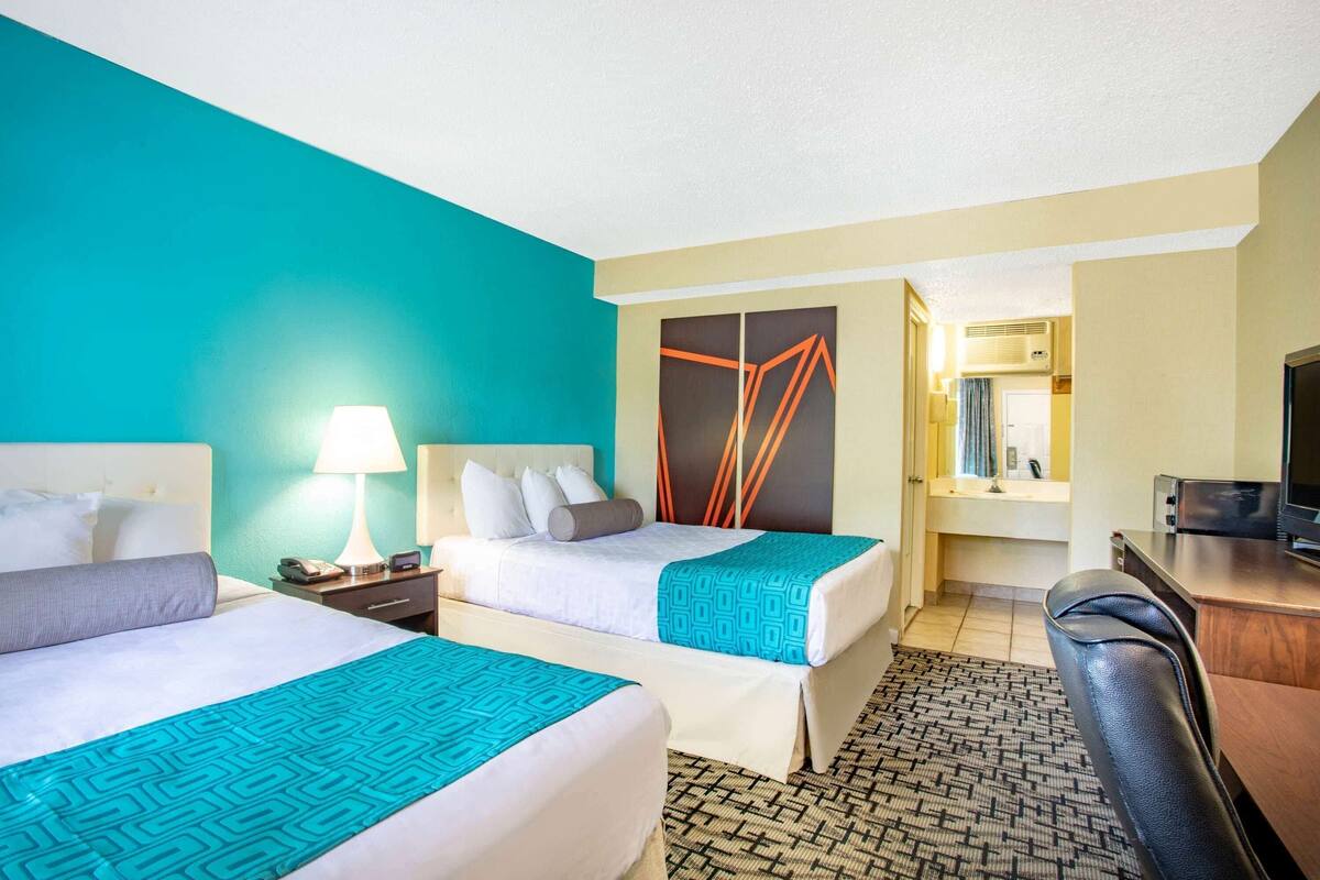 A hotel room with two beds, a desk, a TV, and a bathroom visible through an open door.
