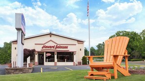 A Howard Johnson motel with a large American flag, a signboard, and a wooden chair in the foreground.