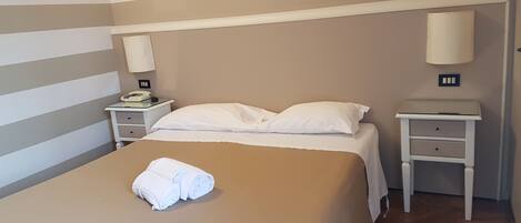 A hotel room with a bed, two bedside tables, a lamp on each table, and a folded towel on the bed.