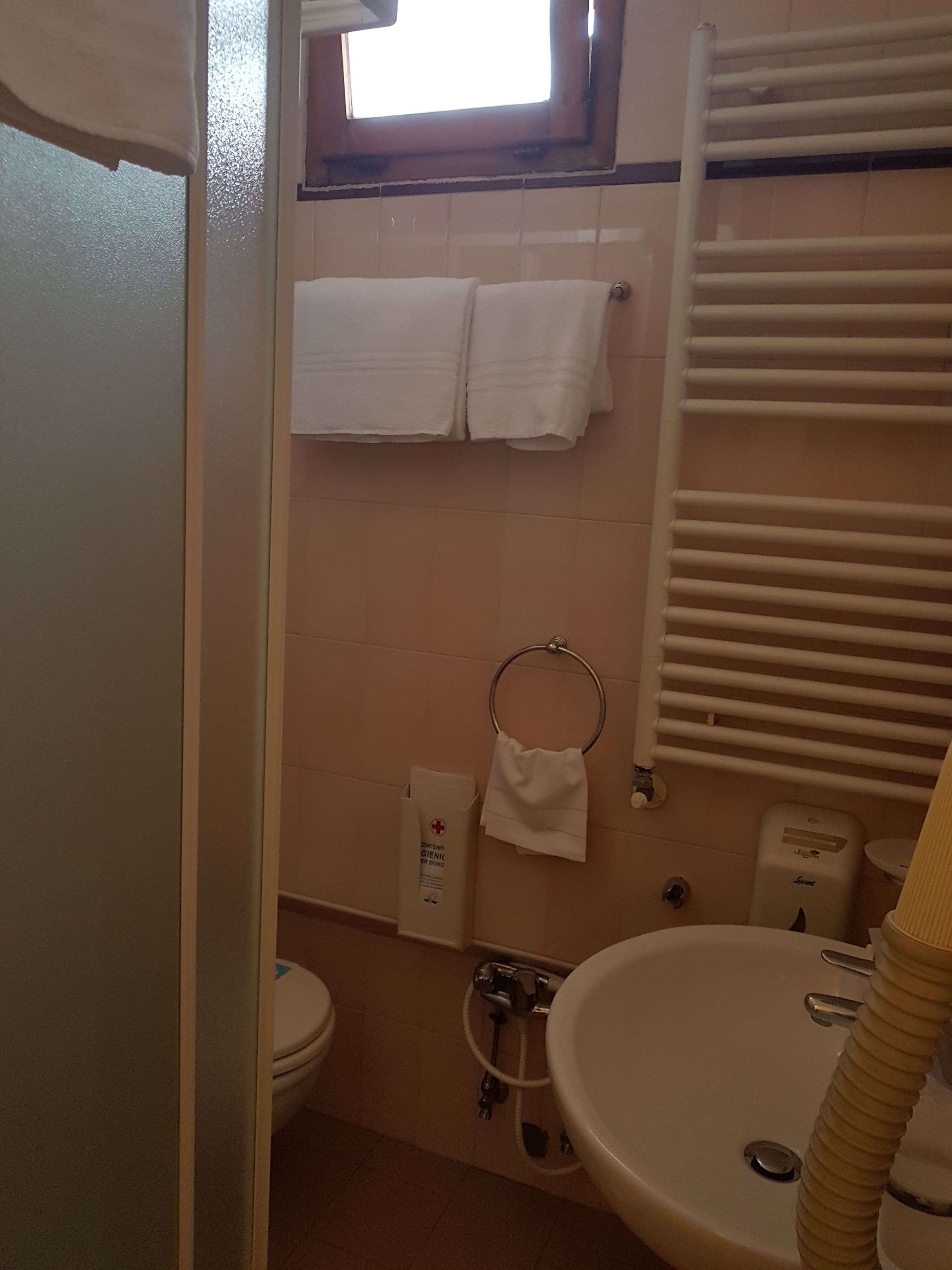 A bathroom with a toilet, sink, towel rack, and a window.
