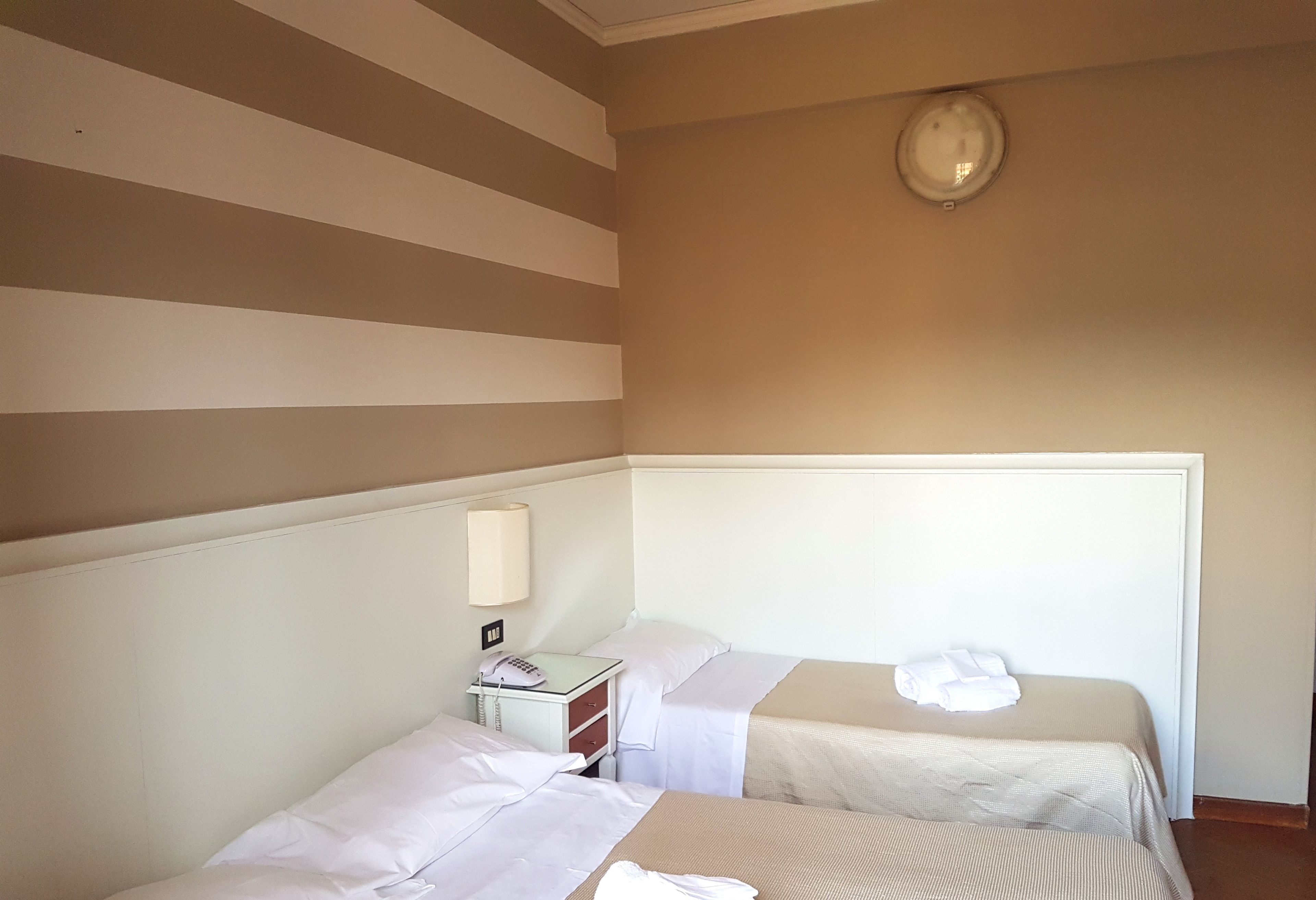 Habitación de hotel con dos camas, una mesita de noche con lámpara y una luz en el techo.