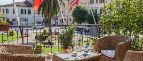 A balcony with wicker furniture and a table set for two, overlooking a street with buildings and a palm tree.