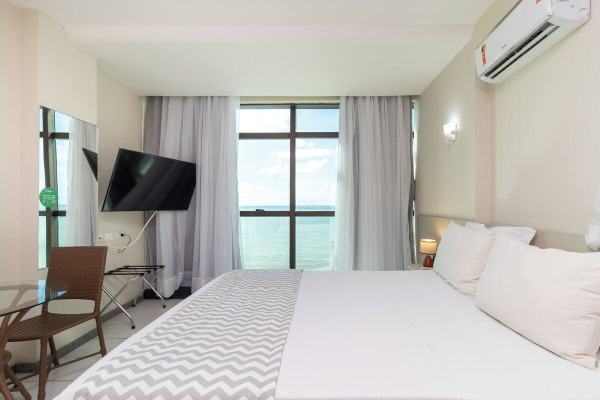 A hotel room with a bed, a TV, a chair, a desk, and a window with curtains.
