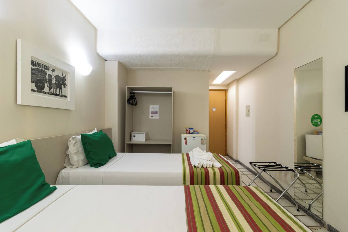 A hotel room with two beds, a small kitchenette, a mirror, and a framed picture on the wall.