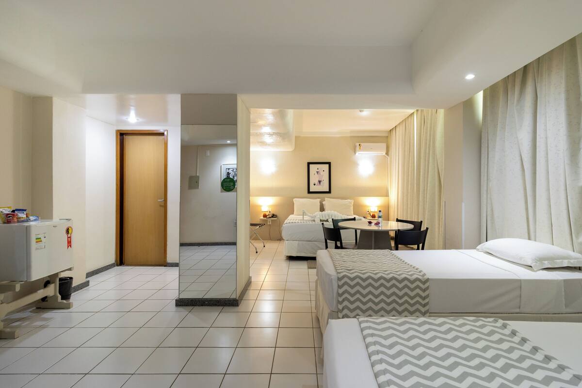 A hotel room with a bed, a desk, a chair, a small table, and a microwave.