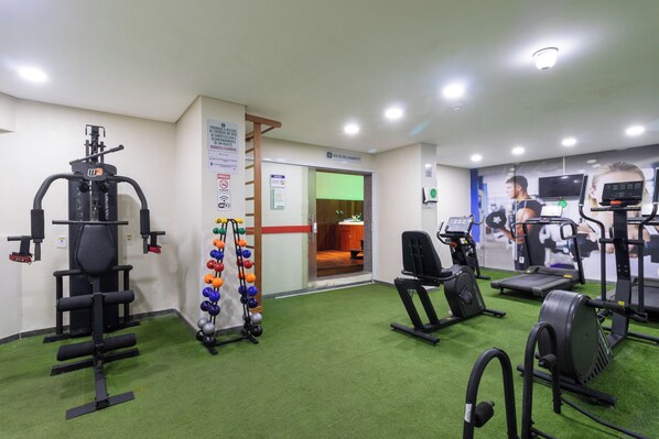 Un gimnasio con diversos equipos de ejercicio, incluyendo cintas de correr y máquinas de pesas, y una pared con pelotas de ejercicio.