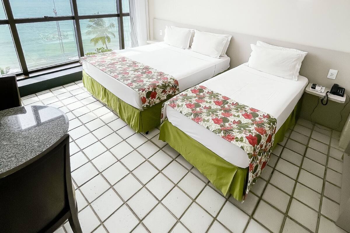 A hotel room with two beds, a desk, and a view of the ocean.