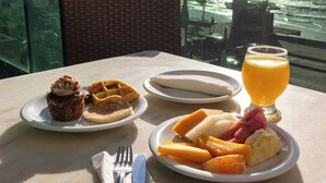 A table with breakfast items and a glass of orange juice, overlooking a body of water. - Hotel Golden Park Recife By Nacional Inn (Recife)