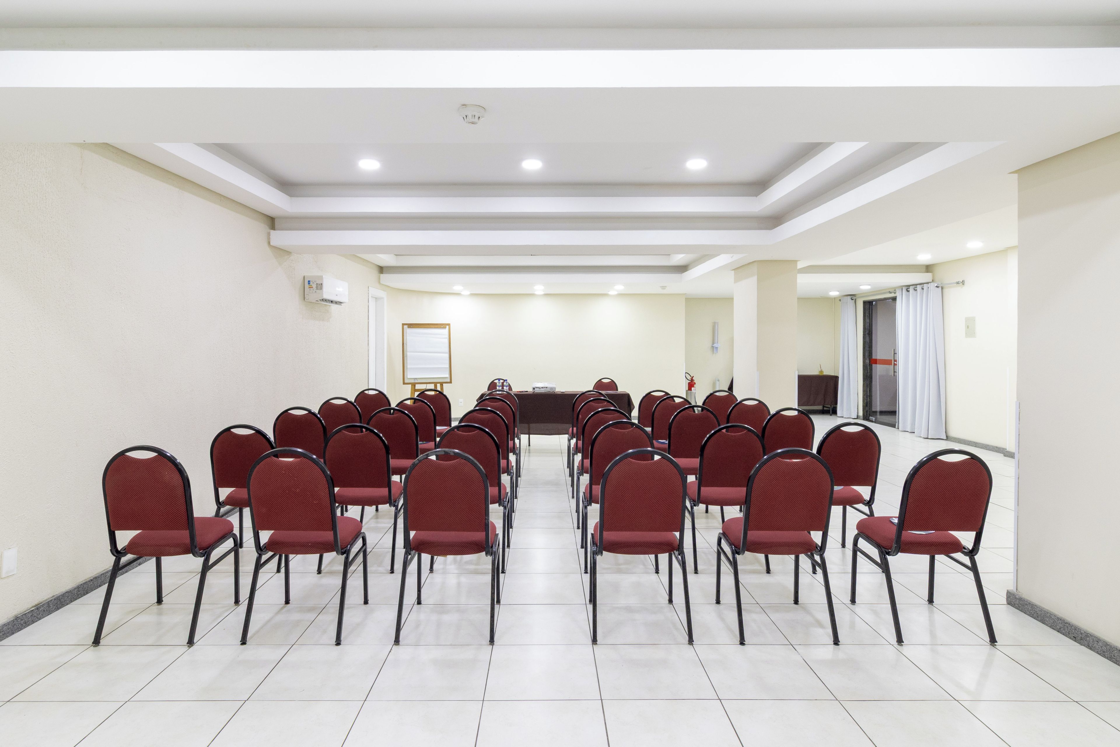 A conference room with rows of chairs facing a long table, white walls, and a ceiling with recessed lighting.