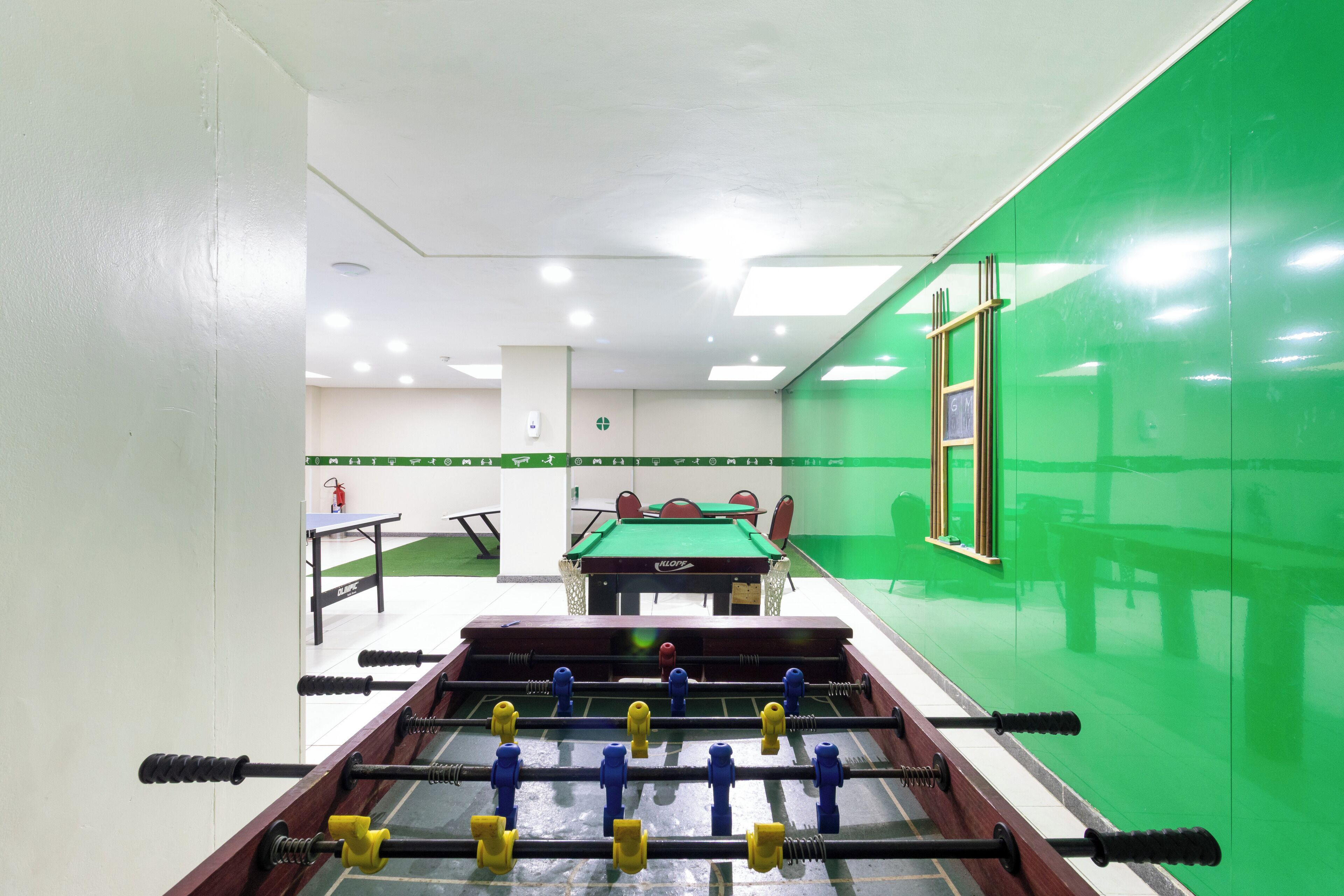A room with a foosball table, a pool table, and a green wall.