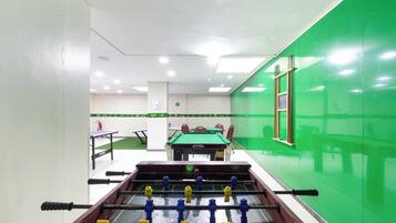 A room with a foosball table, a pool table, and a green wall.
