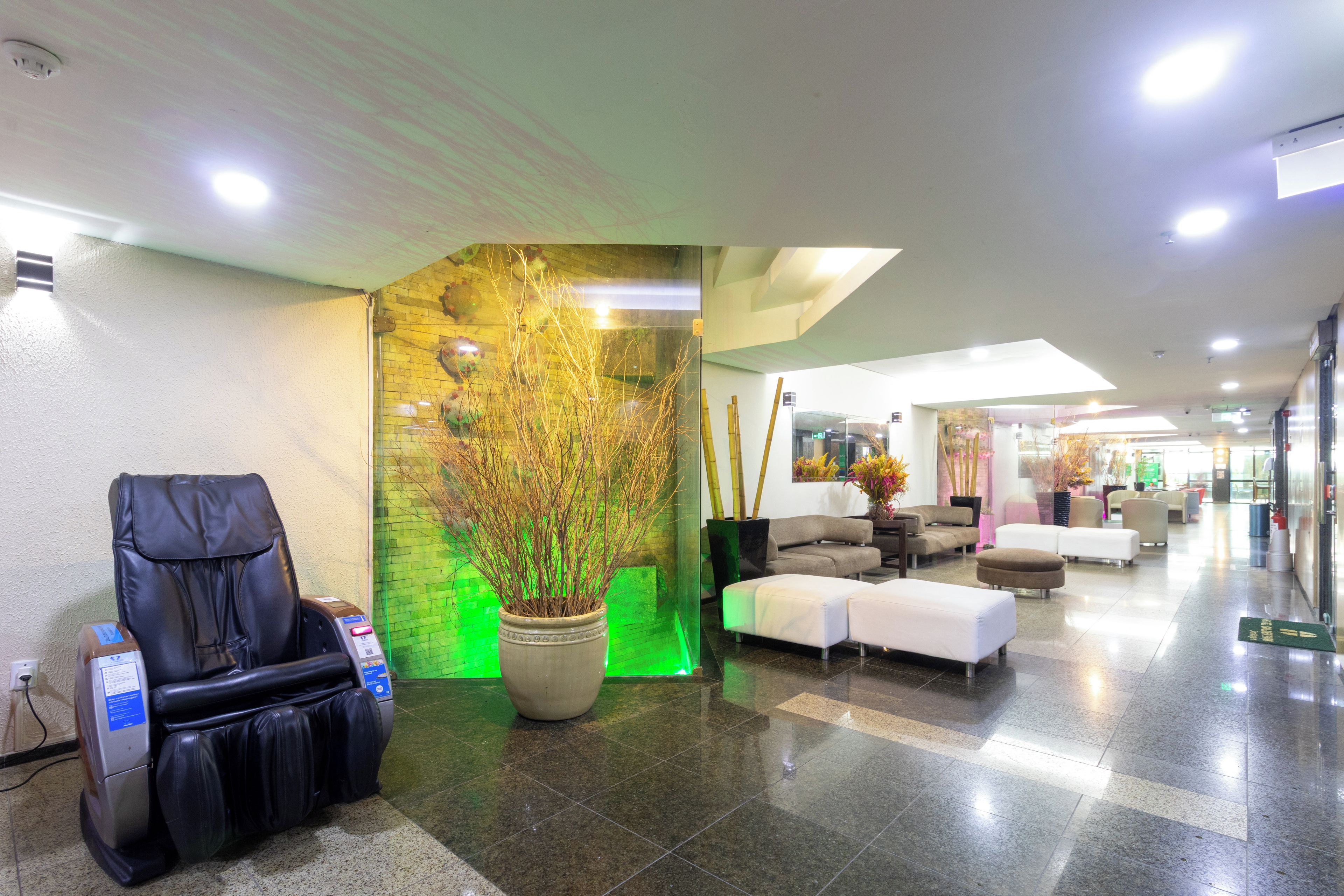 Een hotellobby met een massagestoel, een grote potplant en een zithoek met banken.
