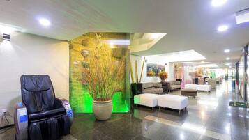 Een hotellobby met een massagestoel, een grote potplant en een zithoek met banken.
