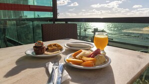 A table with breakfast items including a muffin, waffles, fruit, and orange juice, overlooking a scenic ocean view. - Hotel Golden Park Recife By Nacional Inn (Recife)