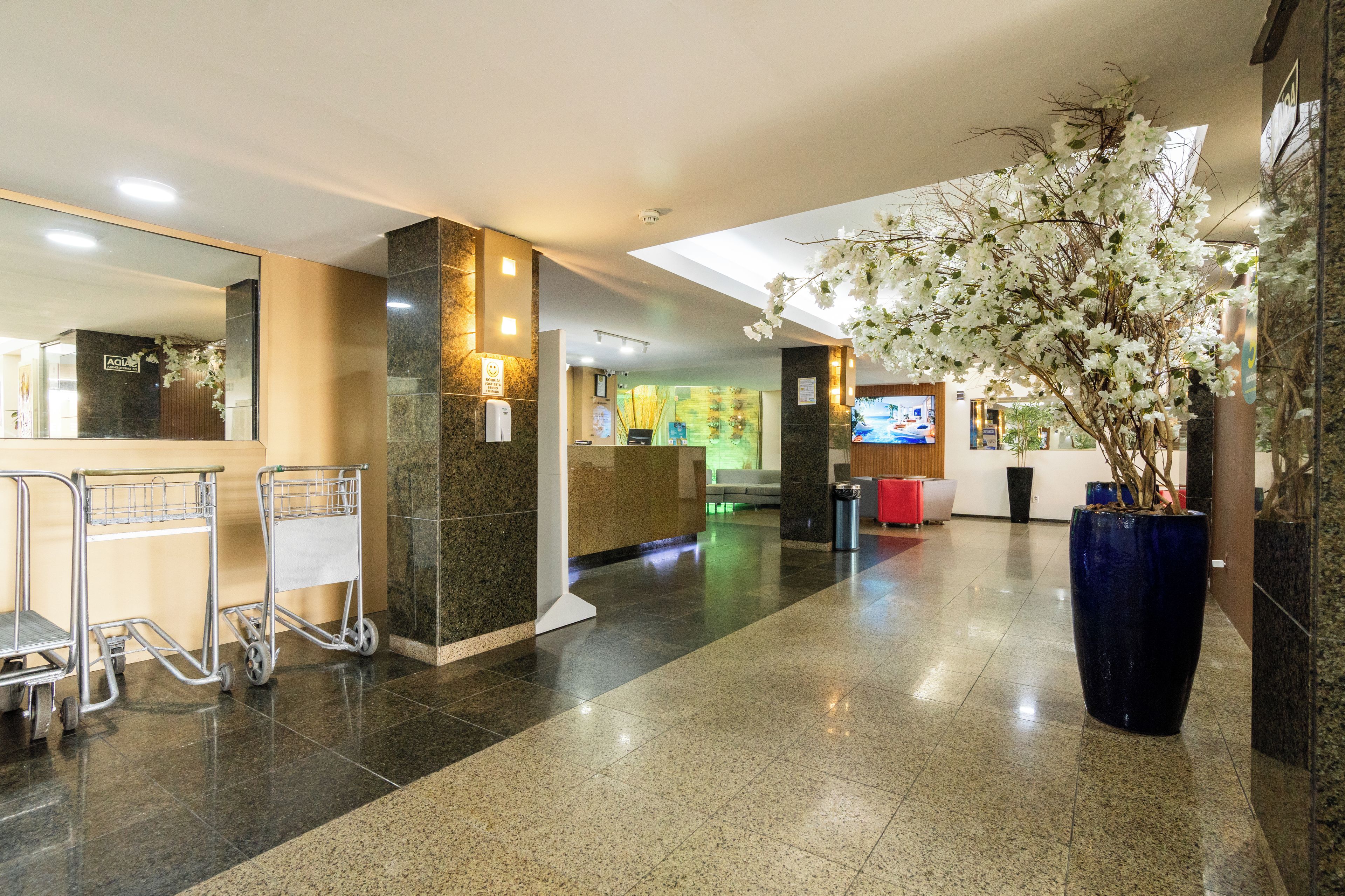 A hotel lobby with a reception desk, a large vase with flowers, and a cart.