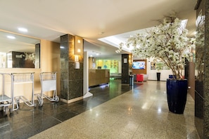 Un hall d’hôtel avec un comptoir d’accueil, un grand vase rempli de fleurs et un chariot.