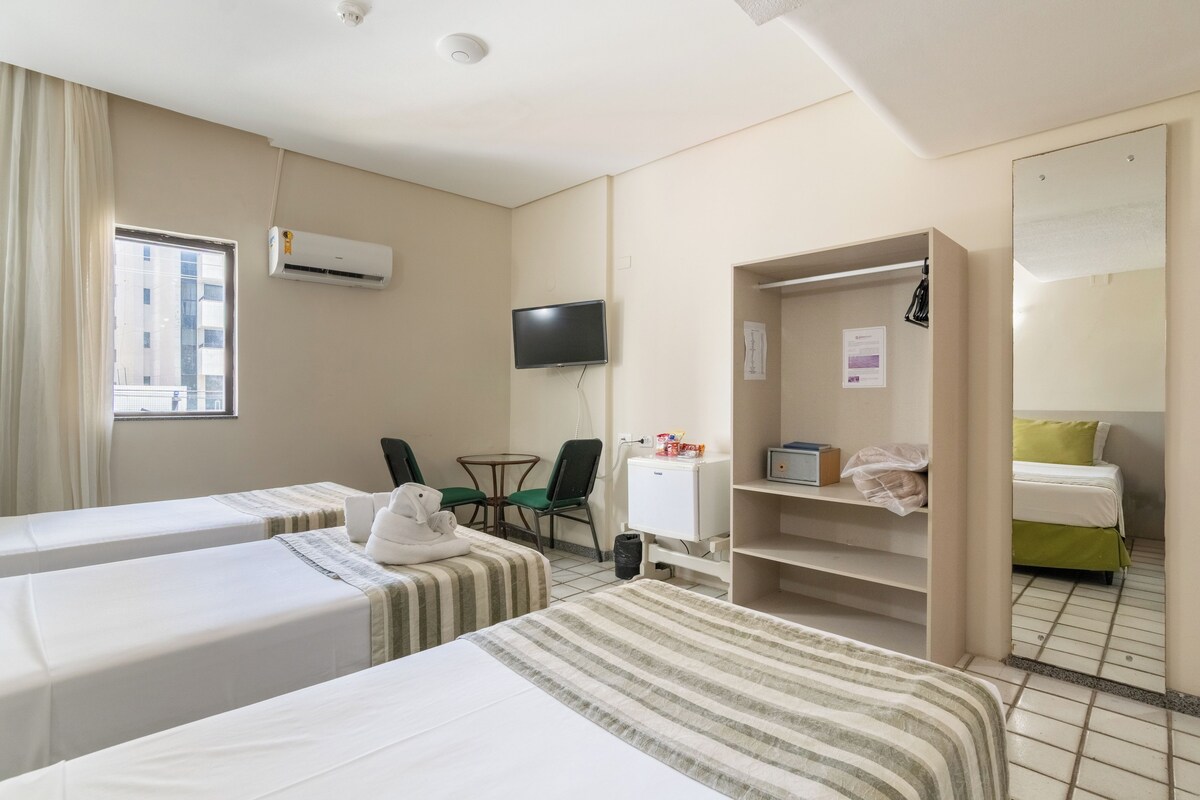 Habitación de hotel con dos camas, televisión, una mesita con sillas, armario y ventana con cortinas.