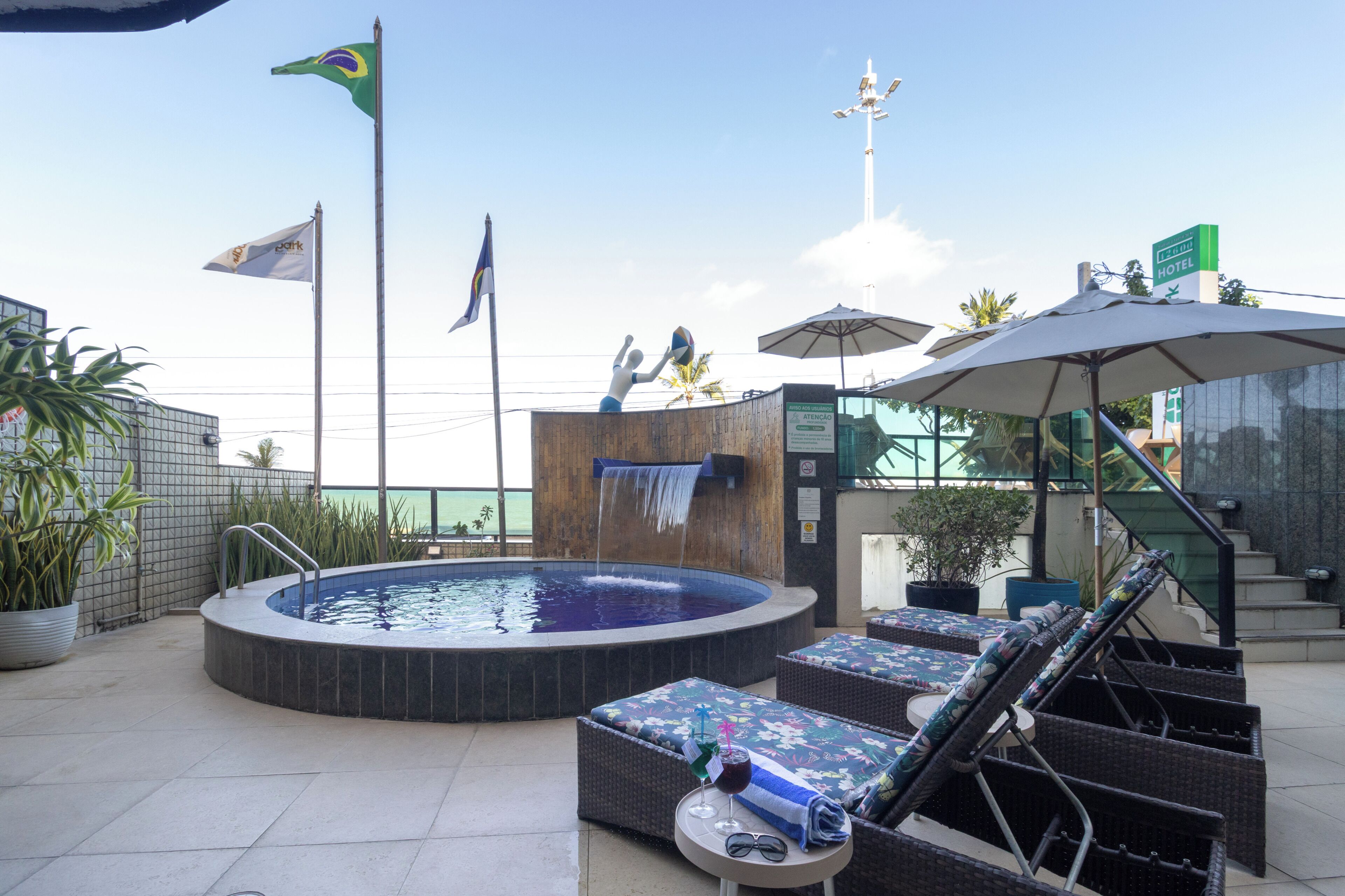 A rooftop pool area with lounge chairs, a hot tub, and flags.