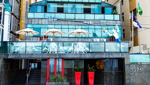 A modern hotel with a glass facade, outdoor seating with umbrellas, and a visible entrance. - Hotel Golden Park Recife By Nacional Inn (Recife)