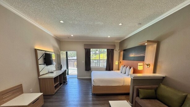 A hotel room with a bed, a sofa, a TV, a desk, and a window.