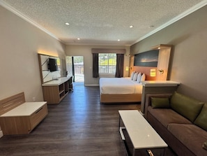A hotel room with a bed, a sofa, a TV, a desk, and a window.