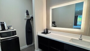 A modern bathroom with a large mirror, a white sink, a black cabinet, and a microwave.