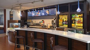 A modern bar area with a long counter, three stools, a coffee machine, and a liquor display.