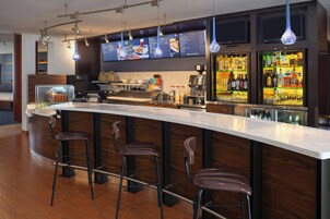 Een moderne bar met een lange toonbank, drie krukken, een koffieapparaat en een drankenkast.