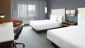 A hotel room with two beds, a desk, a chair, a lamp, and a nightstand with a phone and lamp.