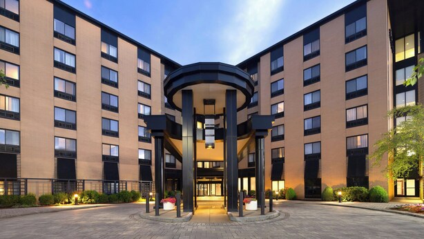 A multi-story hotel with a central atrium, large windows, and a landscaped entrance area.