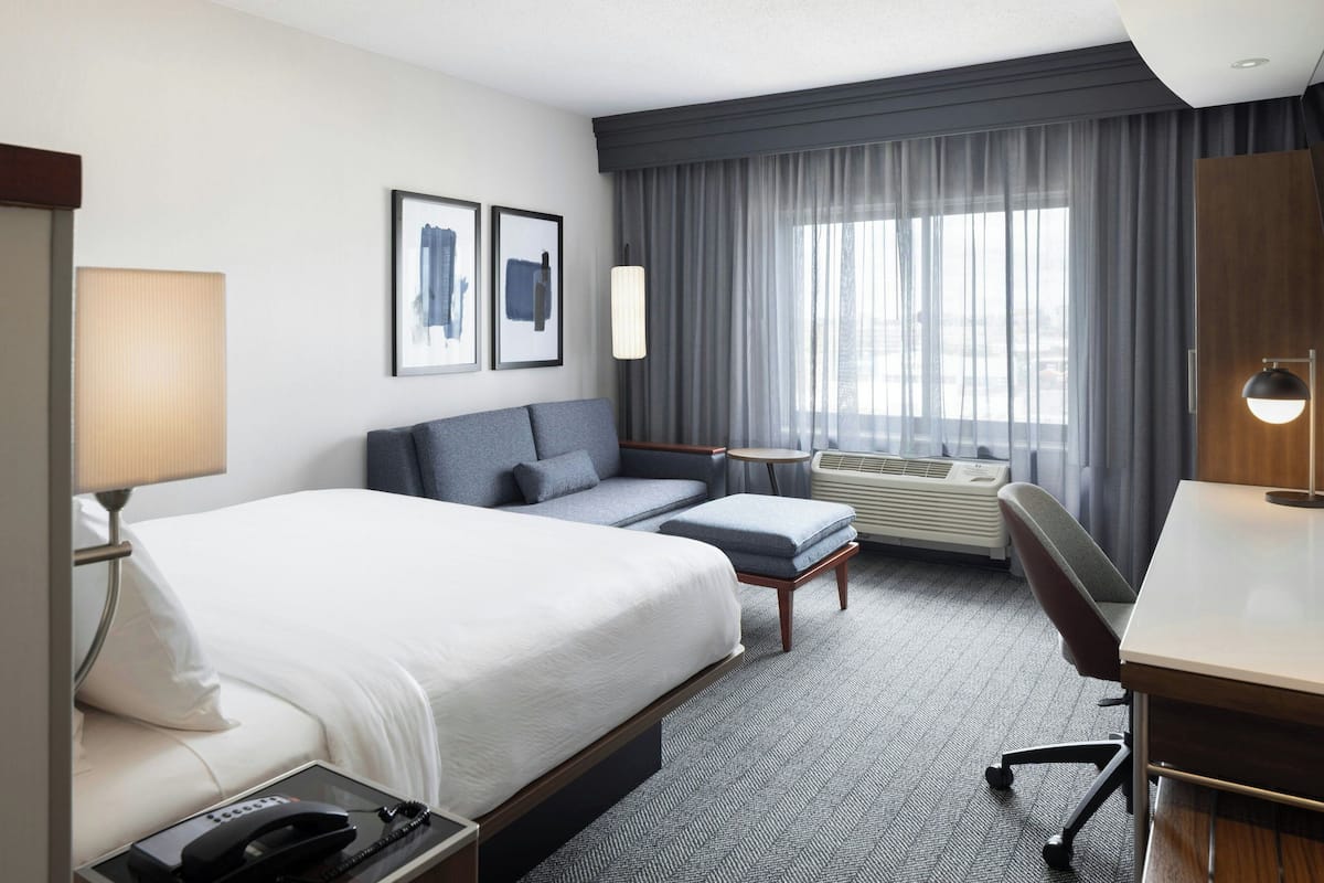 A hotel room with a large bed, a desk, a chair, a sofa, a small table, and a window with curtains.