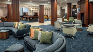 A modern lobby with a curved gray sofa, a bar area, and a seating area with armchairs and ottomans.