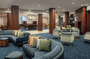 Een moderne lobby met een gebogen grijze bank, een bar en een zithoek met fauteuils en poefs.