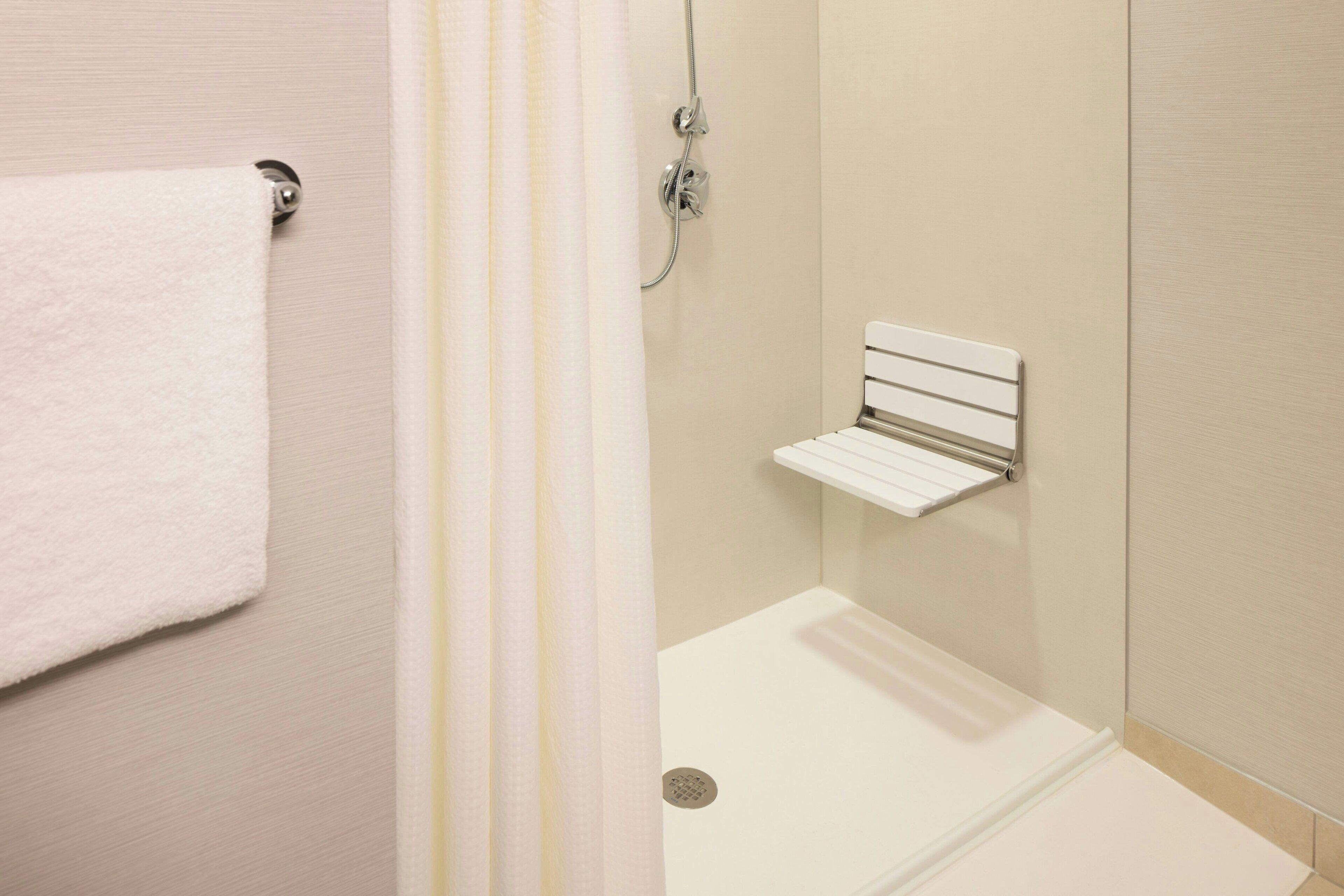 A shower area with a white towel on a hook, a showerhead, and a small shelf.