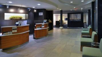 A reception area with two wooden reception desks, a seating area with green upholstered chairs, and a large abstract painting on the wall.