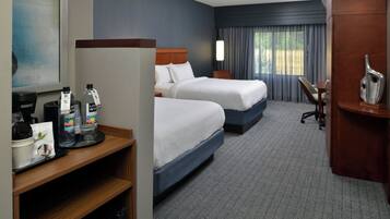 Quarto de hotel com duas camas, uma escrivaninha, uma cadeira, um espaço para café e uma janela grande com cortinas.