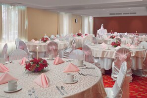 Un salón de banquetes con mesas redondas, manteles blancos y servilletas rosas.