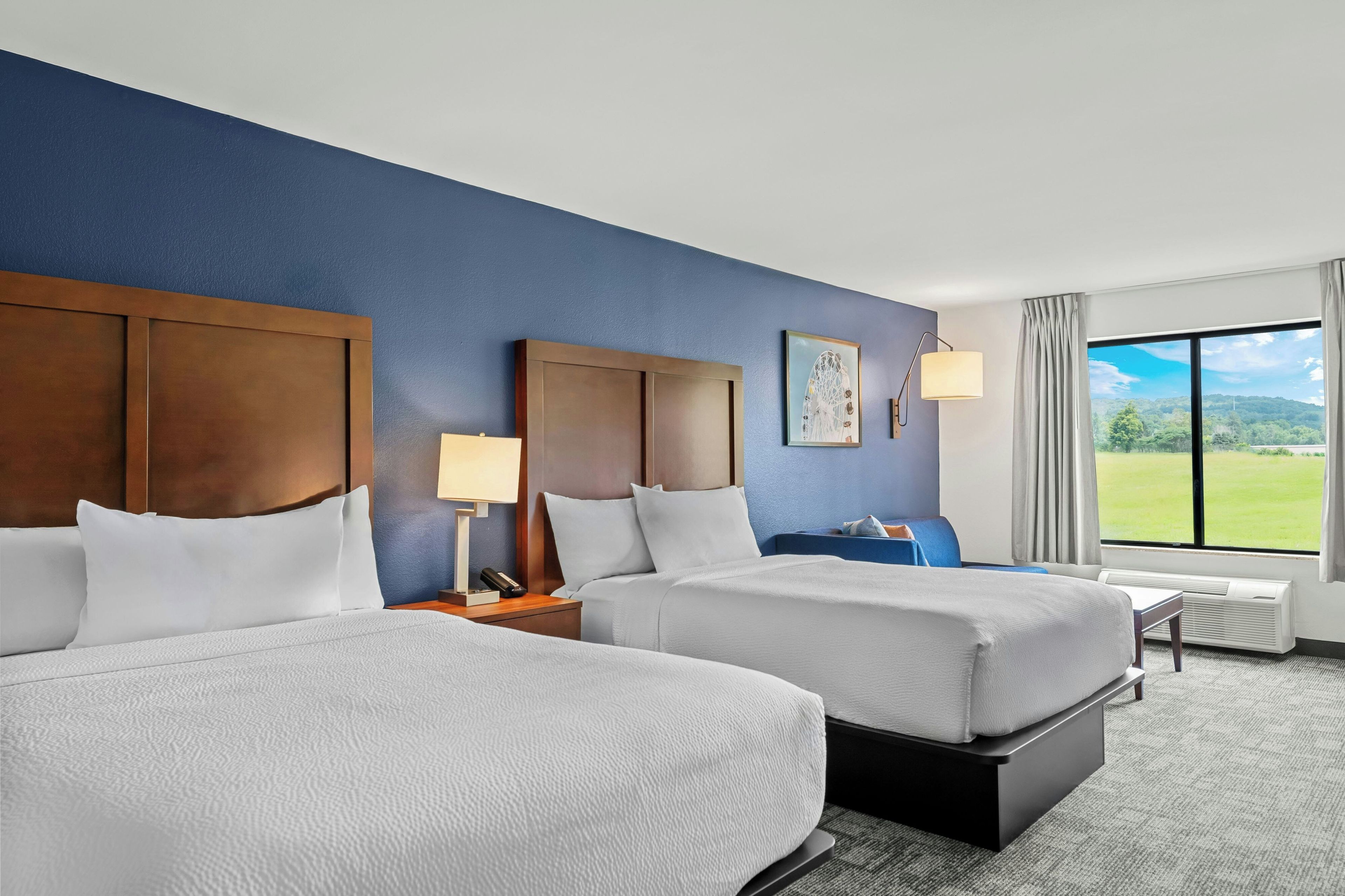 Habitación de hotel con dos camas, un ventanal con vistas a un paisaje verde y una obra de arte colgada en la pared.