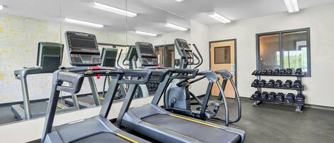 Un gimnasio con cintas de correr, bicicletas estáticas y un estante con mancuernas.