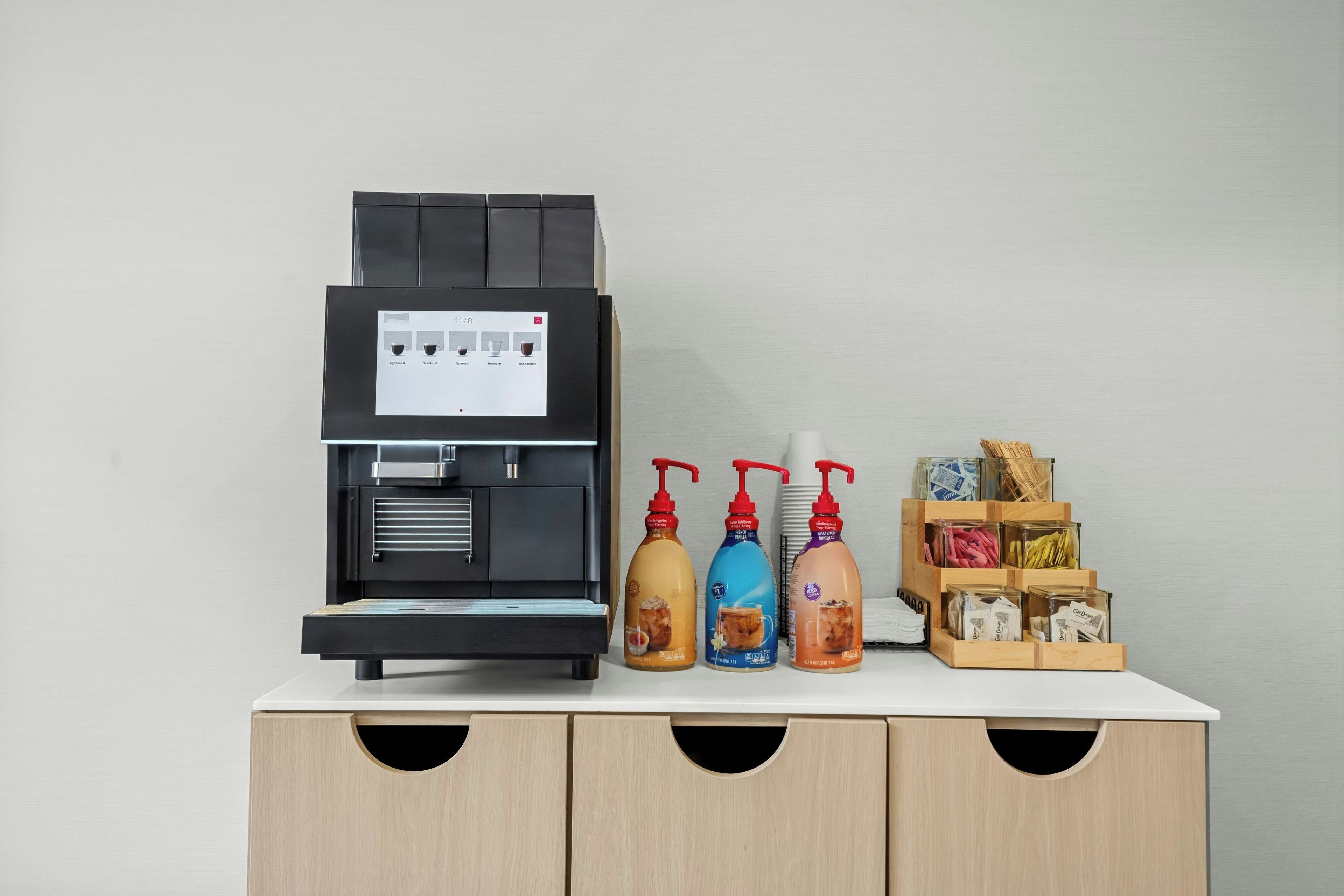 A coffee machine with a digital display, three beverage dispensers, and a wooden storage unit with compartments.