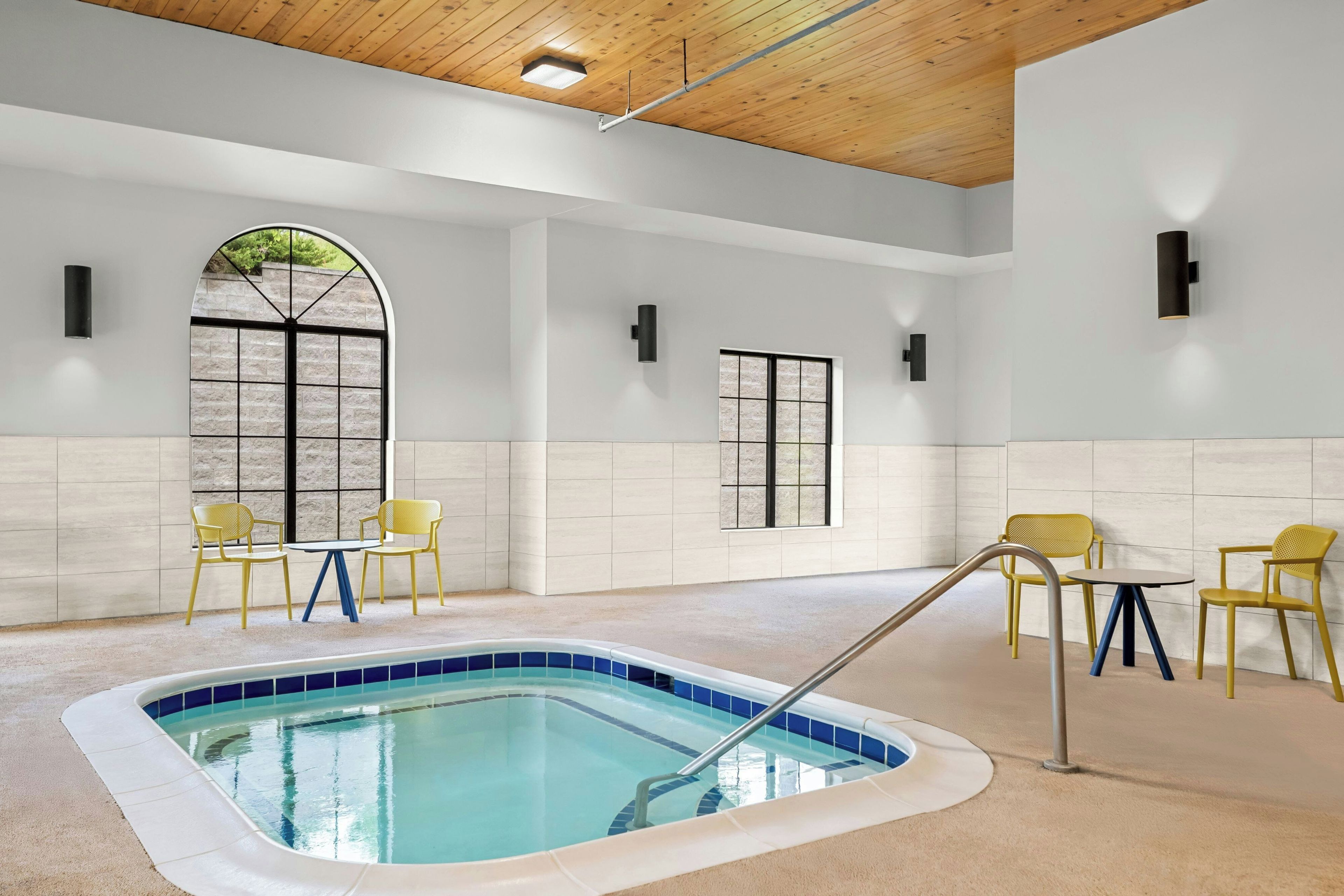 Zona de piscina con un jacuzzi, dos sillas amarillas y una mesa.