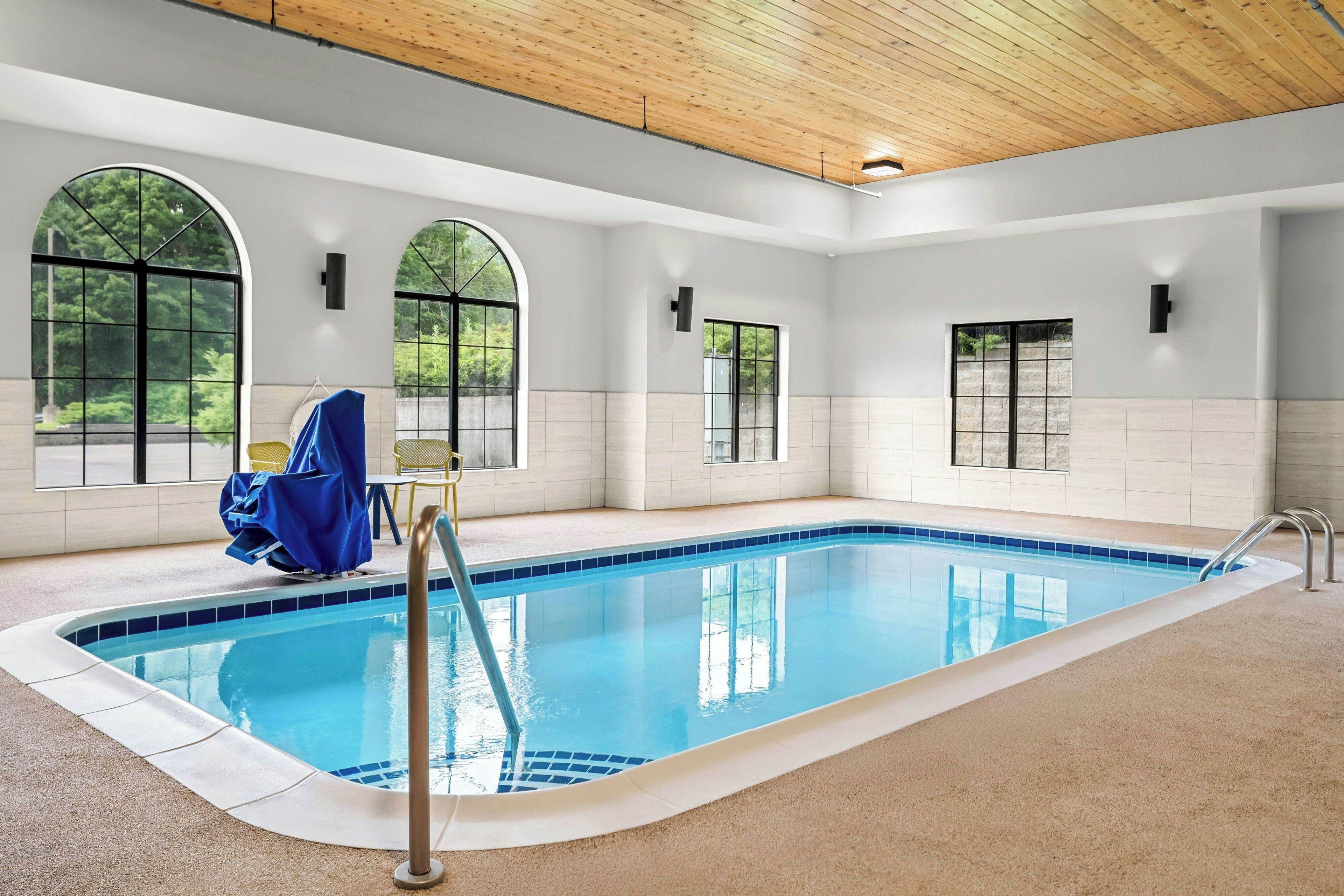 An indoor swimming pool with clear blue water, surrounded by white walls and large arched windows.