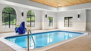 An indoor swimming pool with clear blue water, surrounded by white walls and large arched windows.