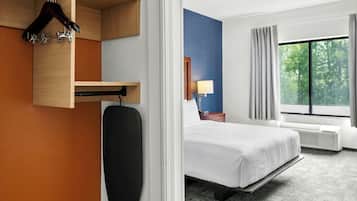 A hotel room with a bed, a bedside table with a lamp, a window with curtains, and a wall-mounted heater.
